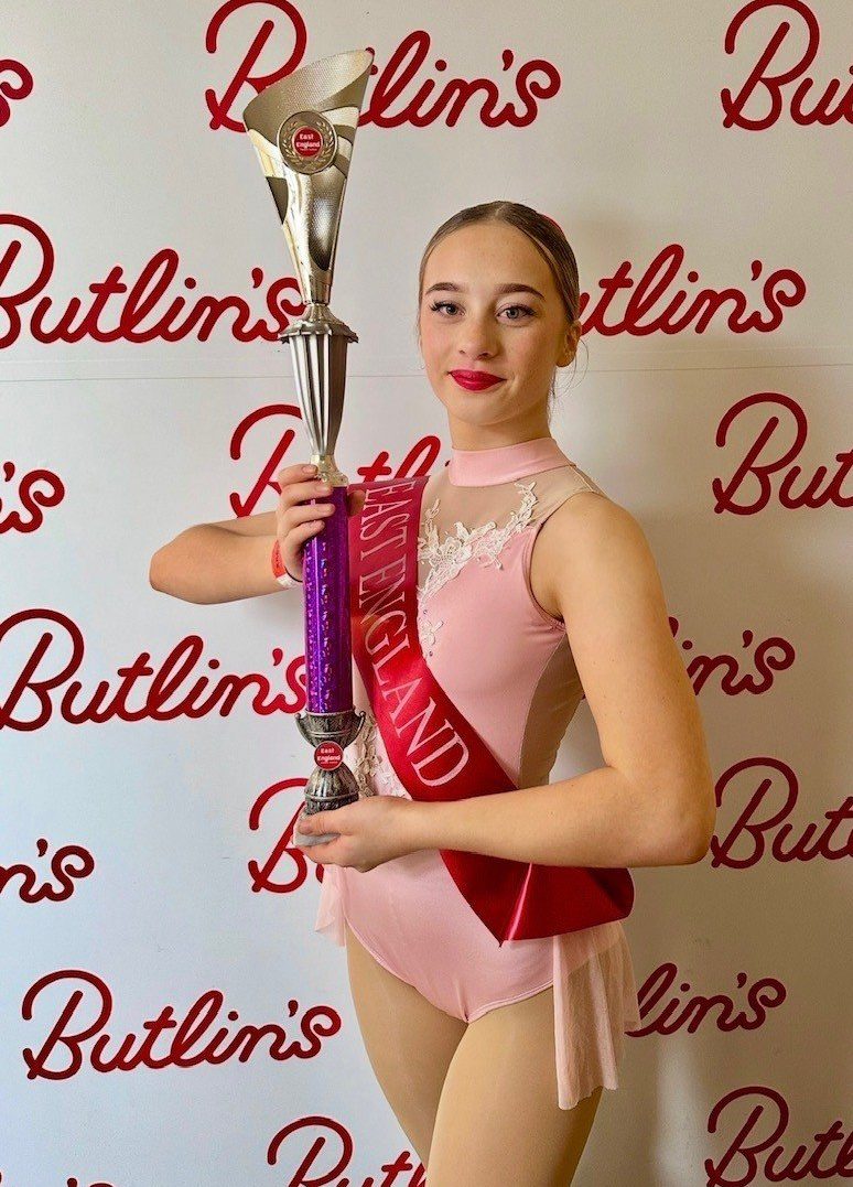 Gracie is stood next to a butlins background in a dance dress, holding a large trophy
